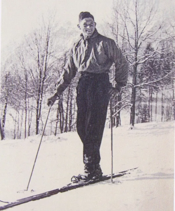 Franz Kniewasser steht lächelnd auf Ski im Schnee, beide Stöcke in den Händen.