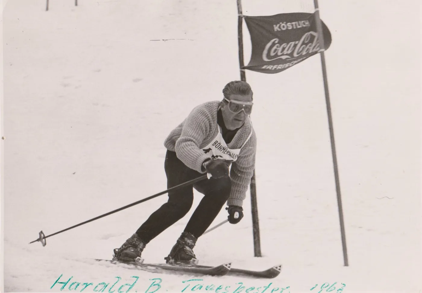 Harald Baumschlager im Strickpullover fährt in tiefer Hocke an einem Tor mit Coca-Cola-Flagge vorbei.